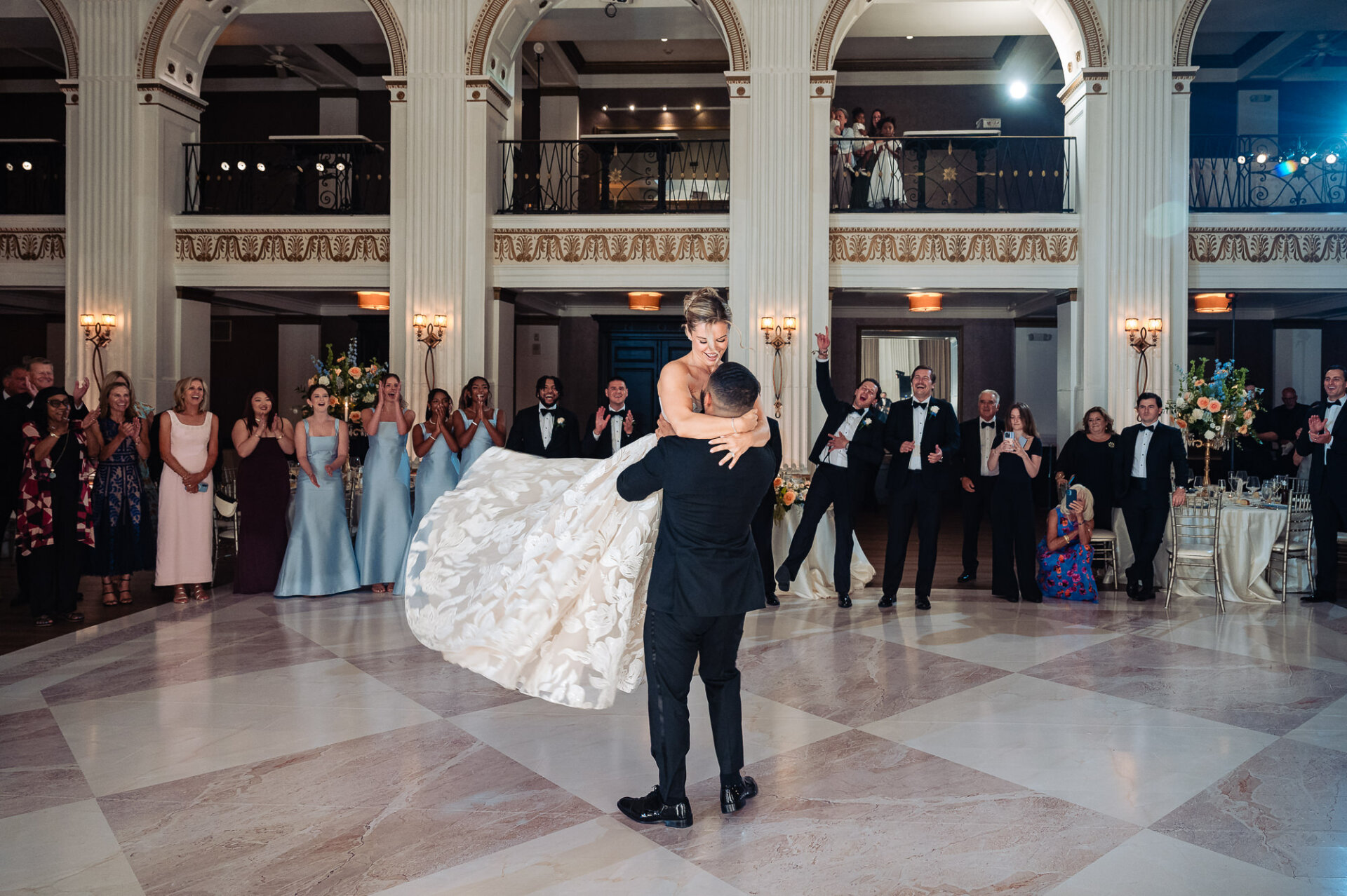 Groom dipping and lifting the bride in the middle of a marble dance floor during their wedding reception at the Ballroom at the Ben while guests cheer.