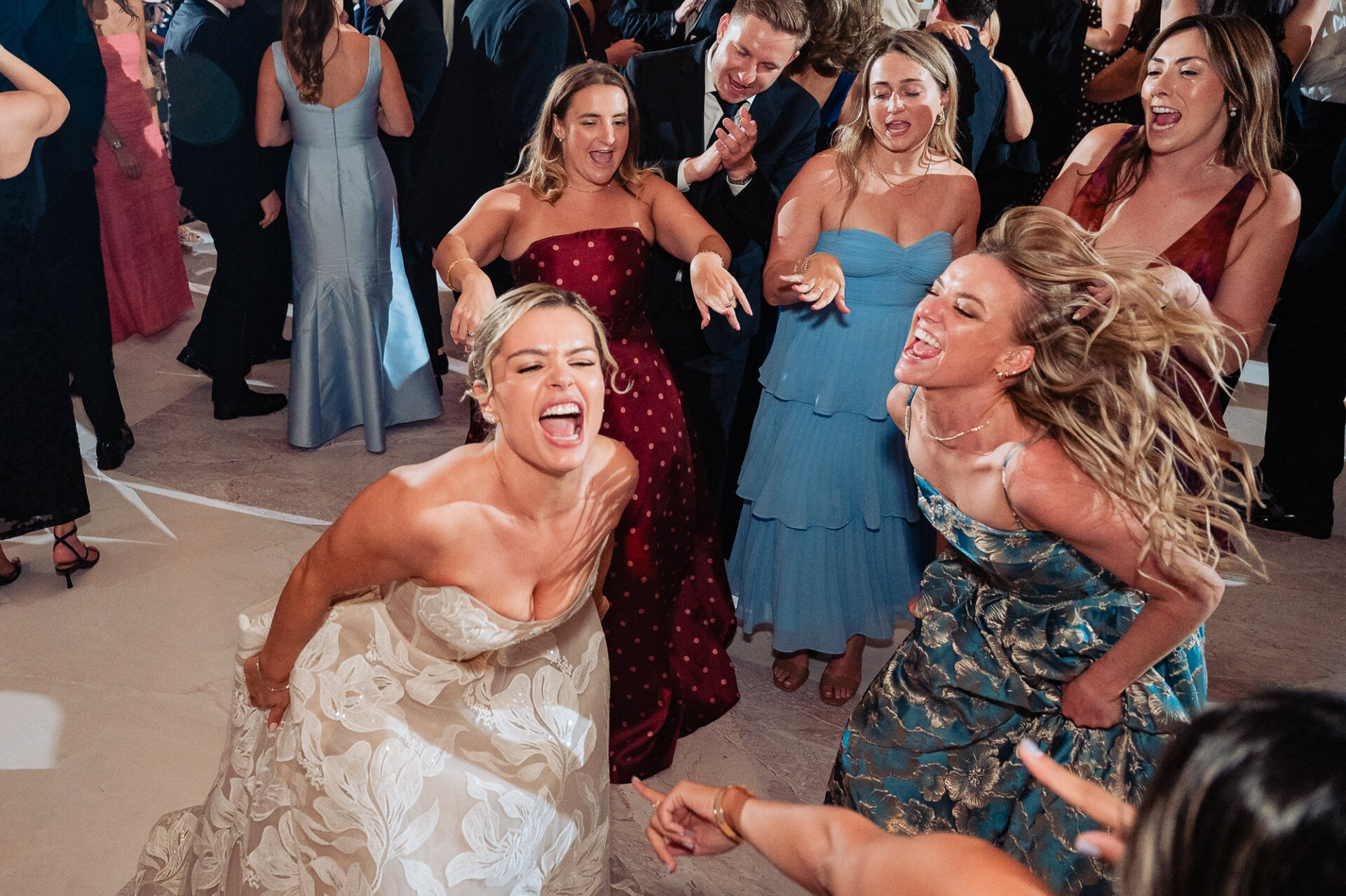 Bride laughing and dancing wildly with her friends in formal dresses on the dance floor during the reception.