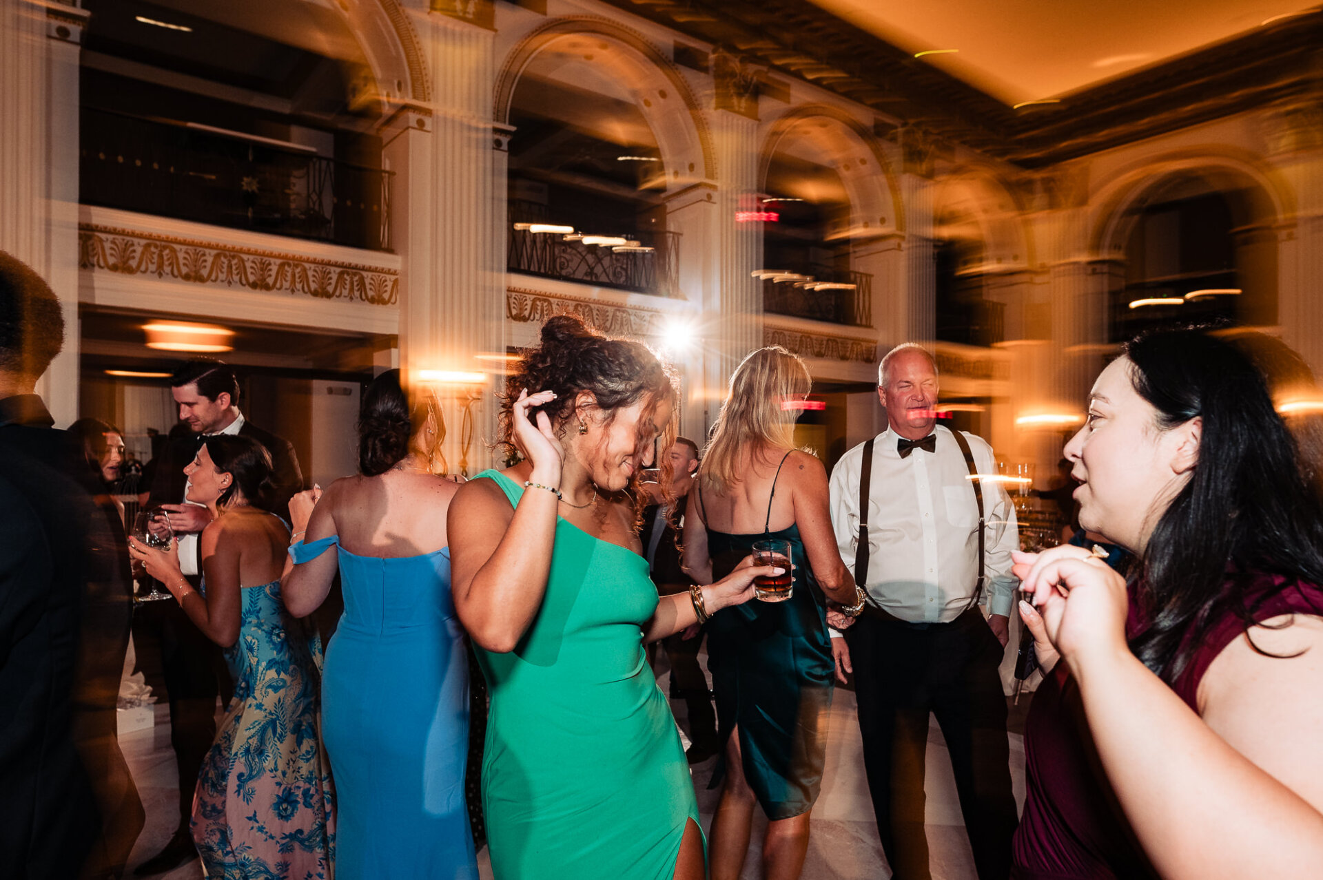 Slow-shutter motion blur photograph of guests dancing on the marble floor inside the venue during the reception.
