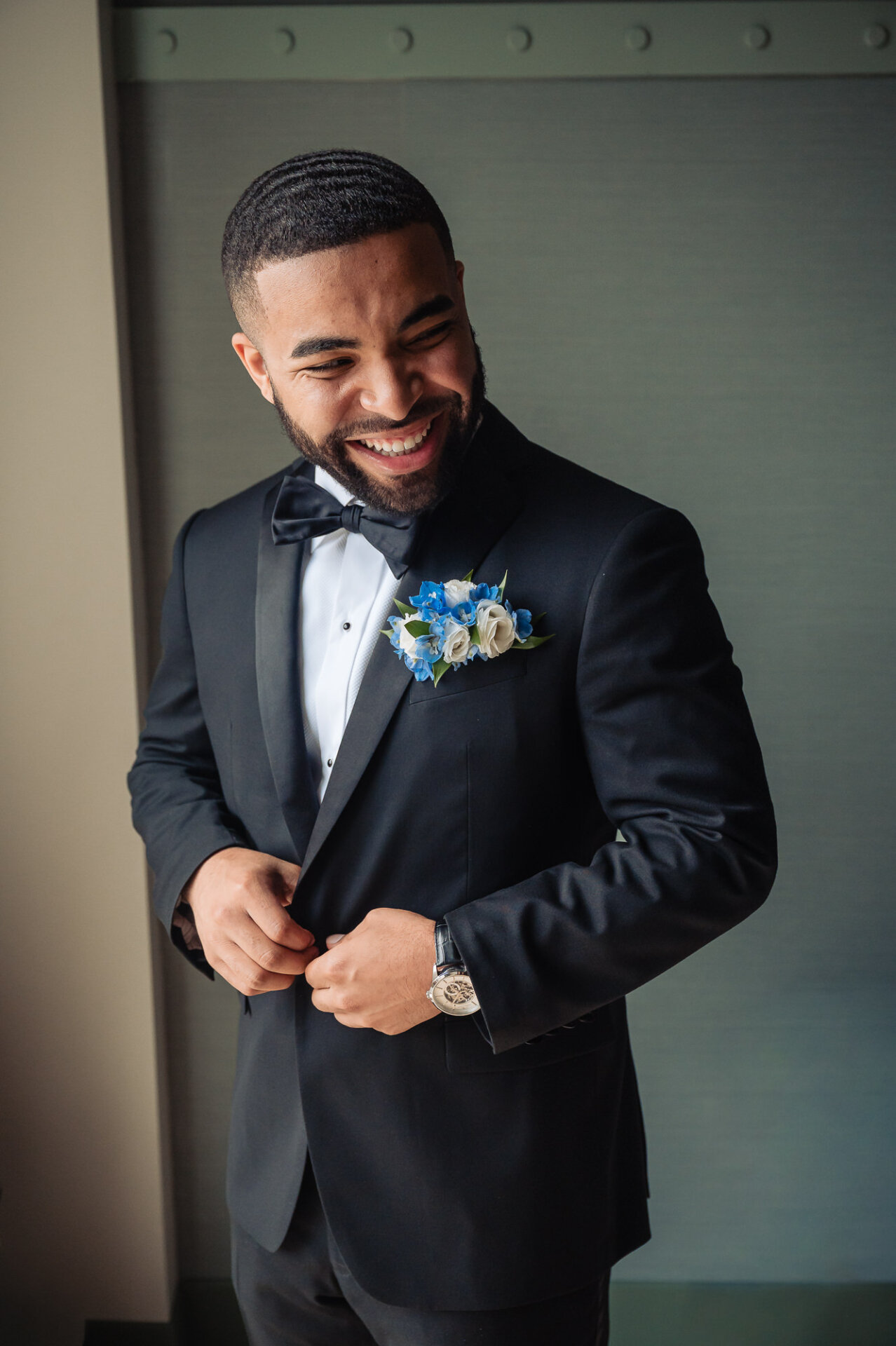 groom smiles in a black tuxedo with a blue-and-white boutonniere before his wedding at The Ben Philadelphia.