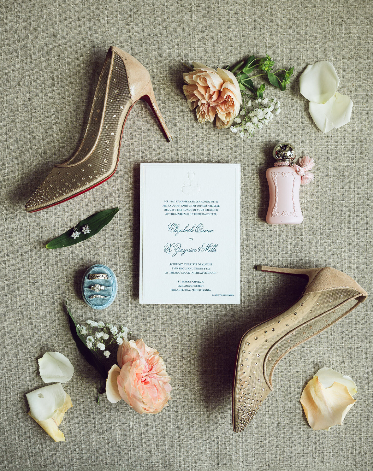 Wedding invitation, rings, rhinestone heels, perfume, and flowers arranged for a Philadelphia wedding.