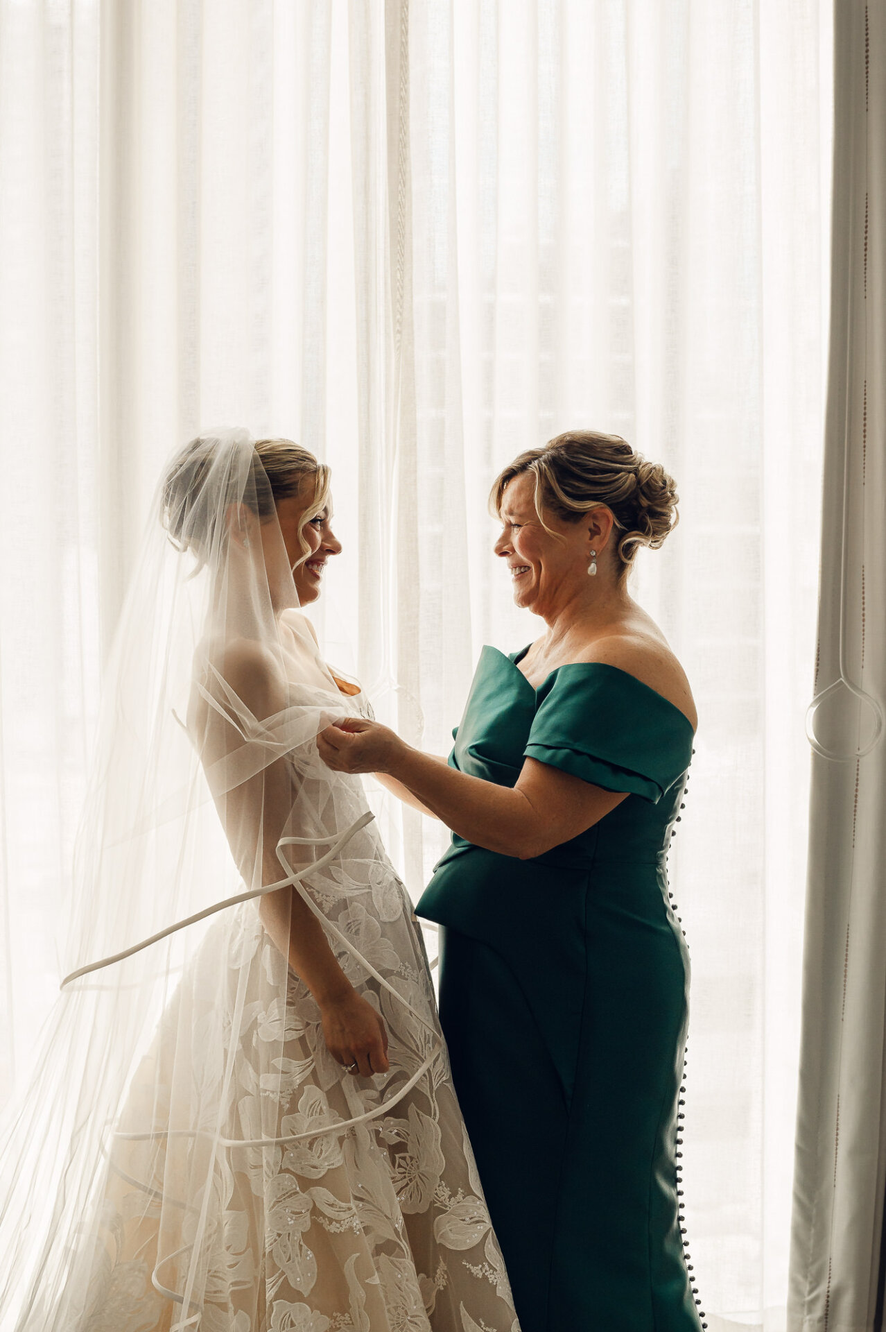 bride's .mother adjusts her veil as they share a smile before the wedding ceremony