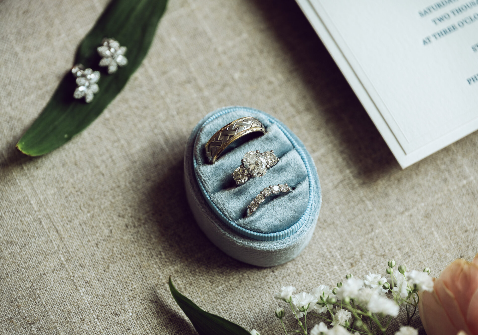 couple's wedding rings displayed in a blue velvet box beside floral earrings and flowers