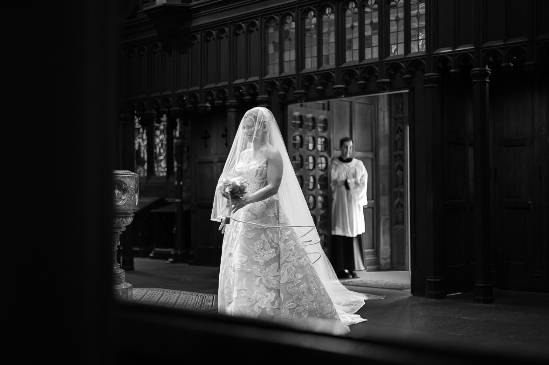 Bride carries her bouquet through Saint Mark’s Church in a black-and-white wedding portrait.