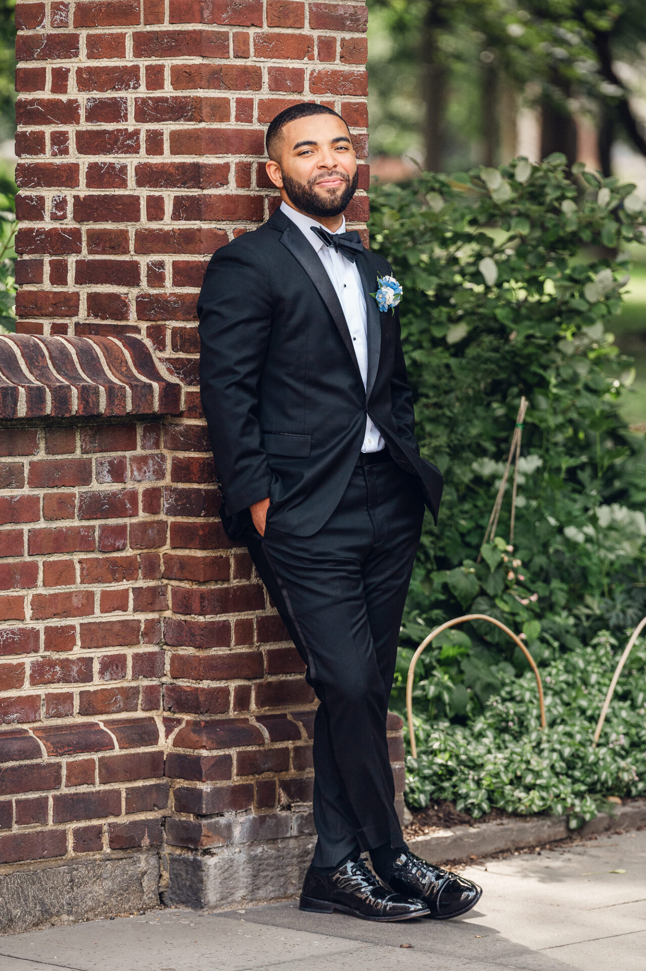 Groom poses in a black tuxedo beside a brick wall before the wedding at The Ben Philadelphia.