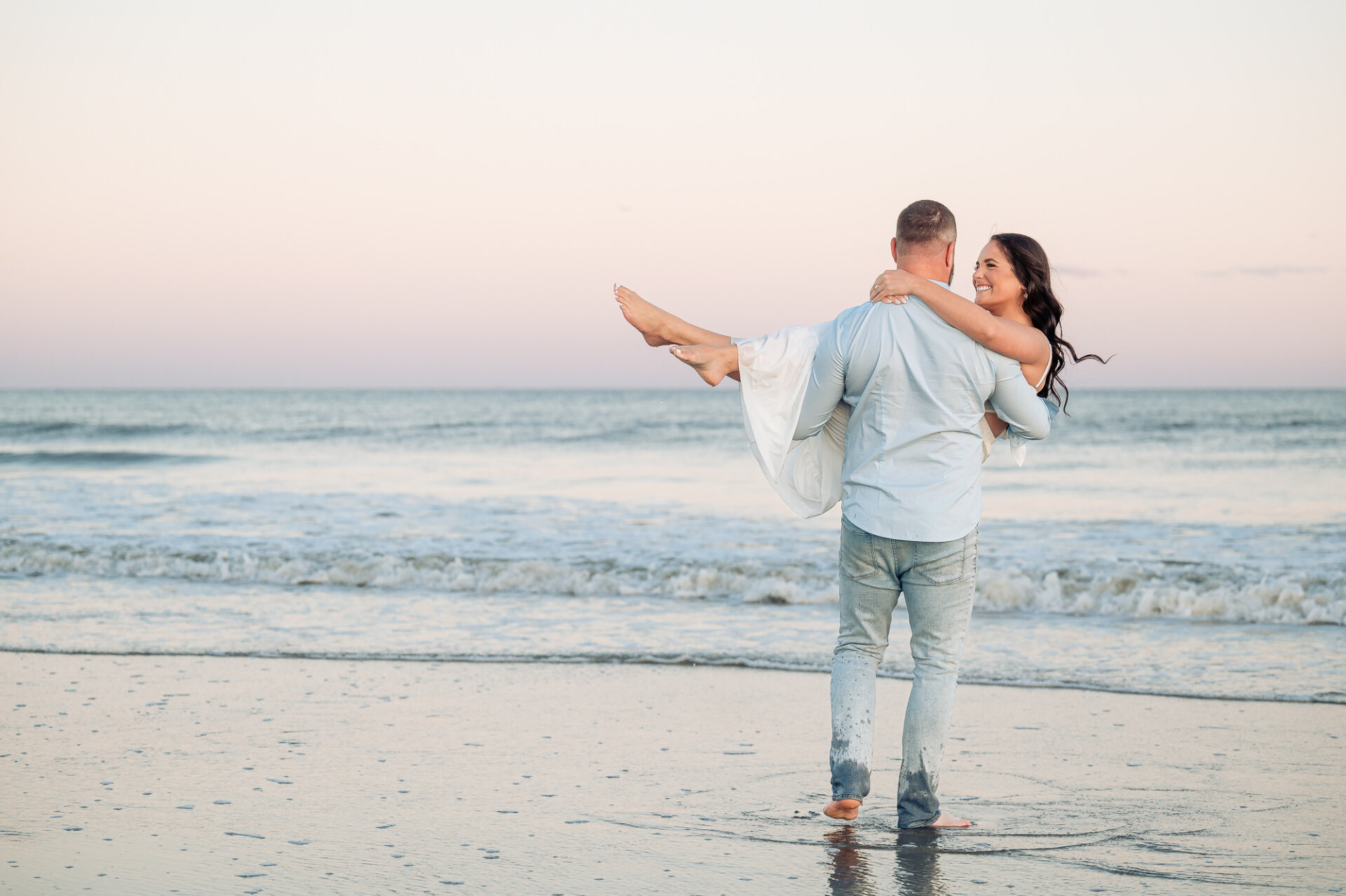 Couple smiling as the man carries his partner along the shoreline during their sunset Margate Beach engagement photoshoot