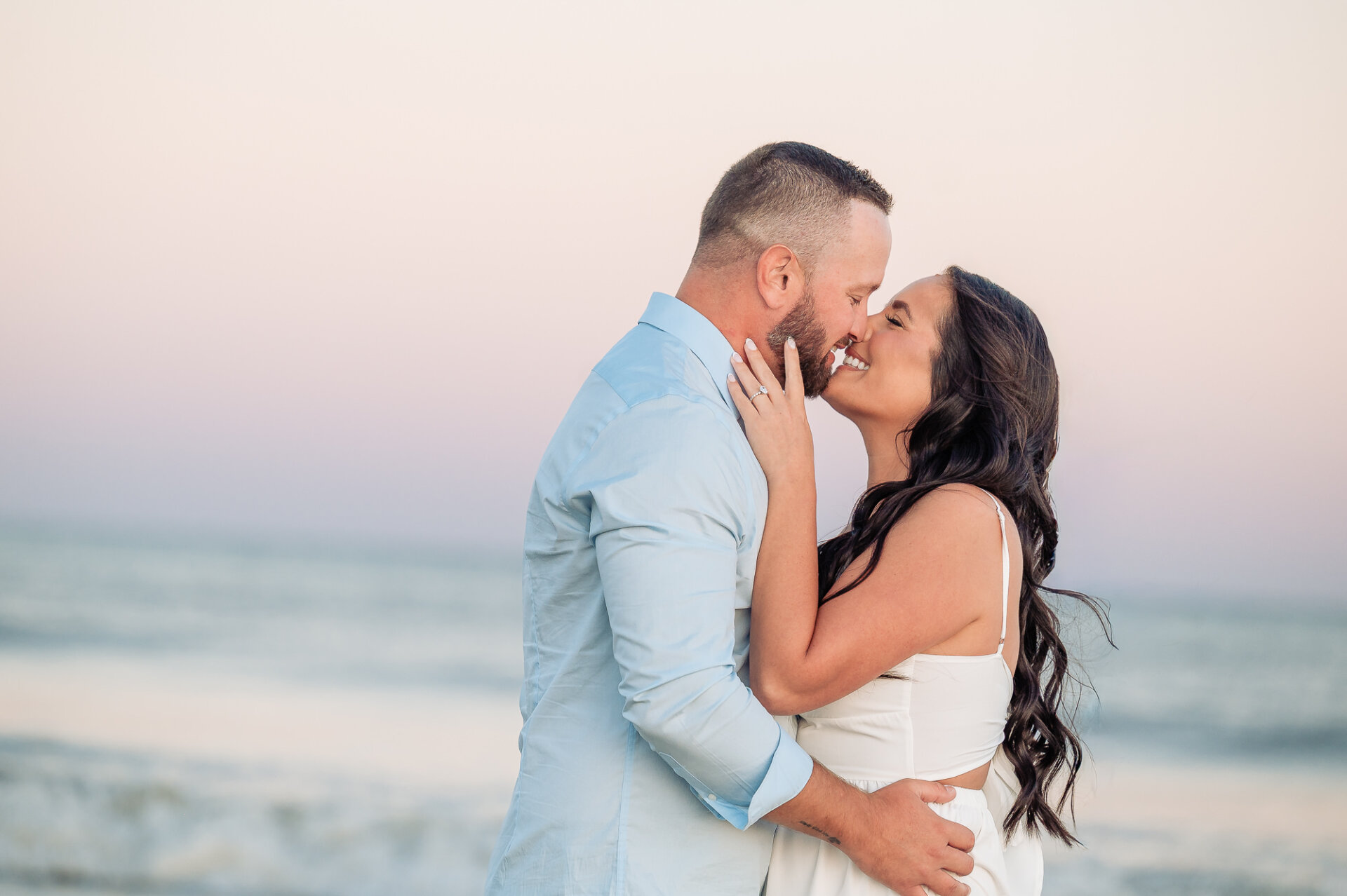 Couple sharing a romantic kiss while embracing by the ocean during their Margate Beach engagement session in New Jersey
