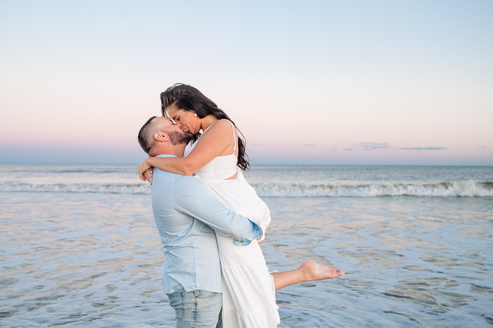 Man lifting his partner into his arms as they kiss during their Jersey Shore beach engagement session