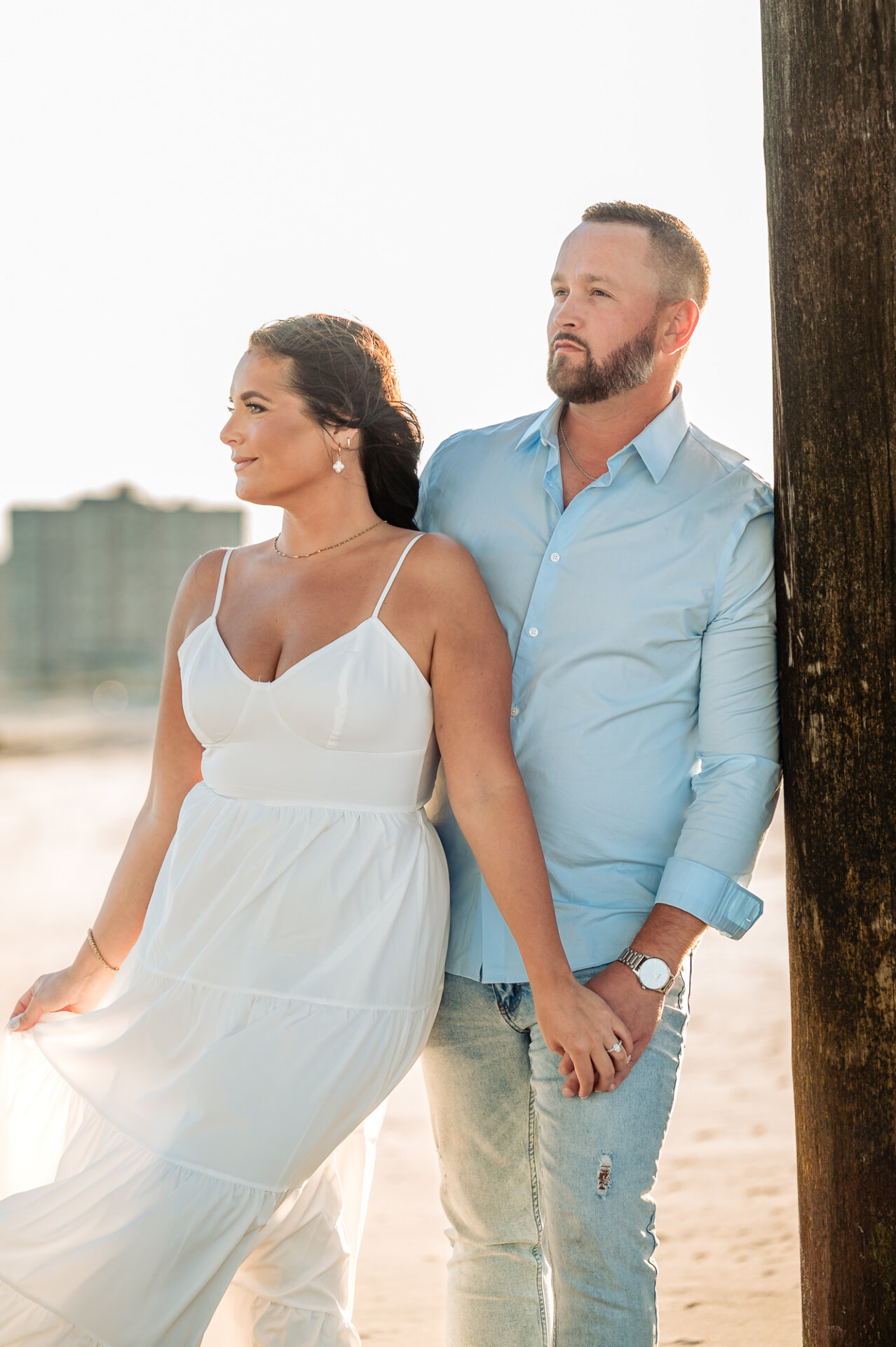 Couple holding hands beside a wooden pier post during their Margate Beach engagement session in New Jersey