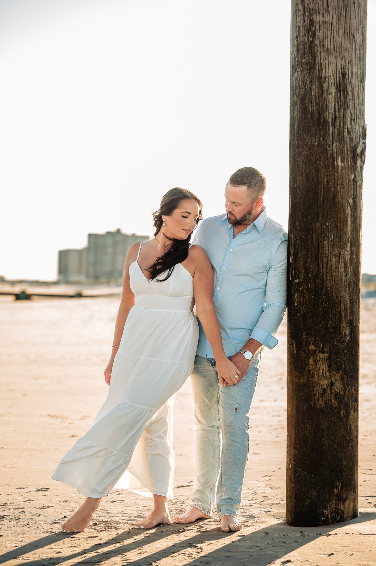 Full-length engagement portrait of a couple leaning against a wooden post on Margate Beach