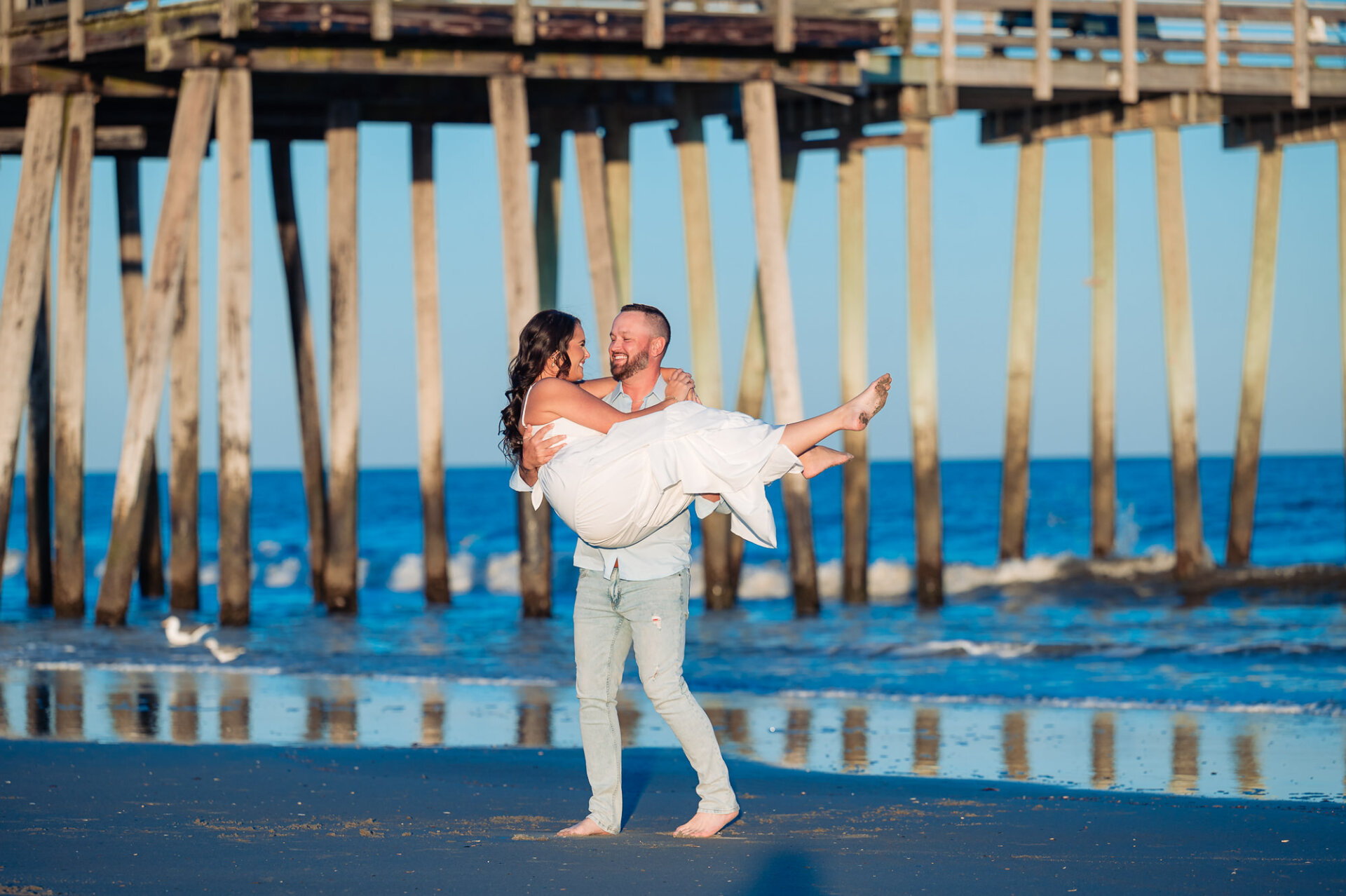 Man lifting his partner in his arms beneath a wooden pier during their Margate Beach engagement photoshoot