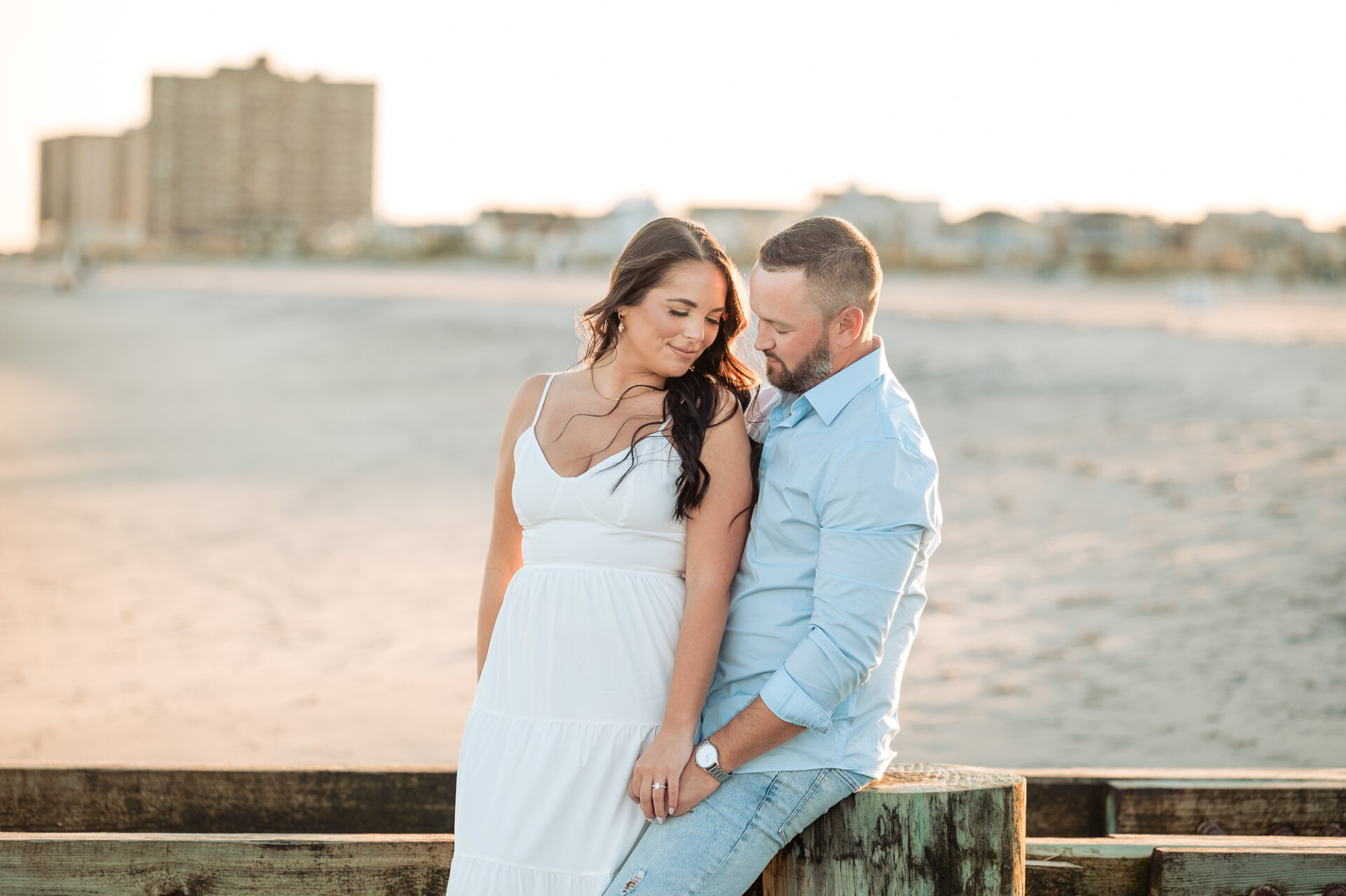 Couple holding hands beside a wooden railing with the sandy Jersey Shore in the background