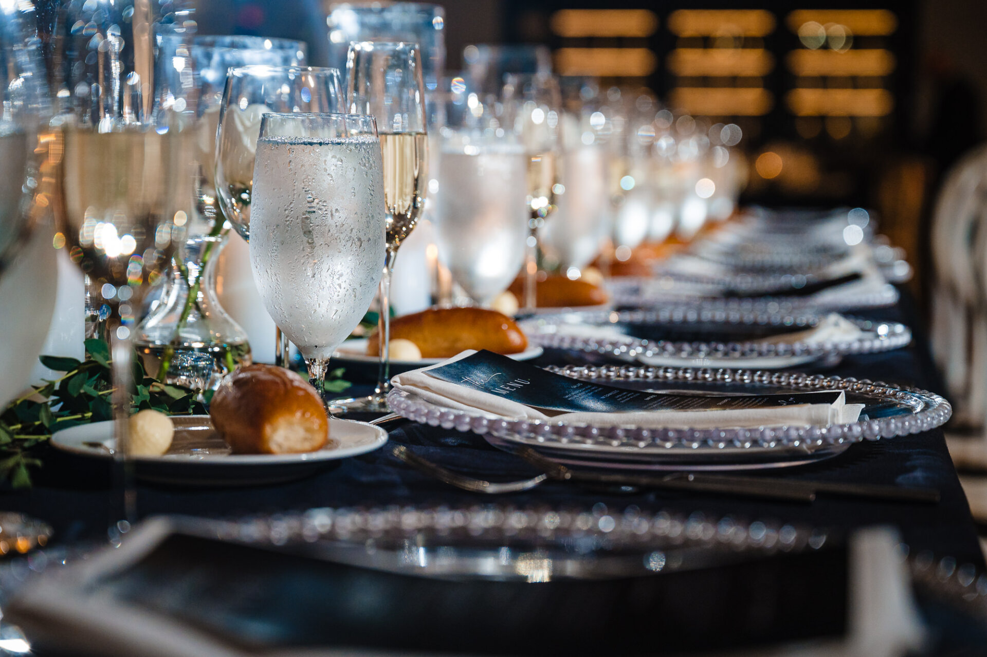 Close-up low-angle view of formal place settings with beaded glass charger plates and water glasses