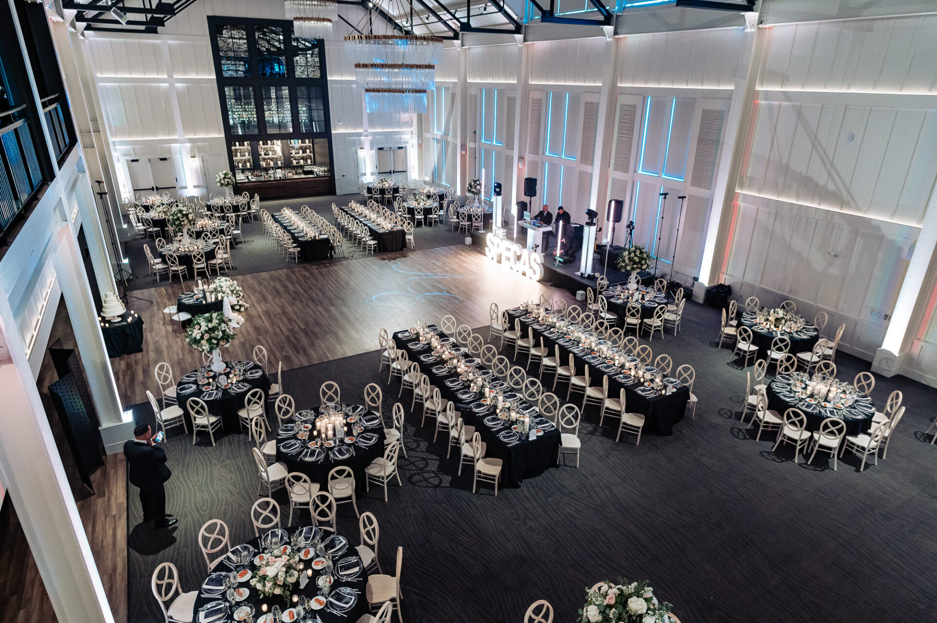 Overhead wide view of spacious wedding reception hall with round dining tables, dance floor, and marquee sign