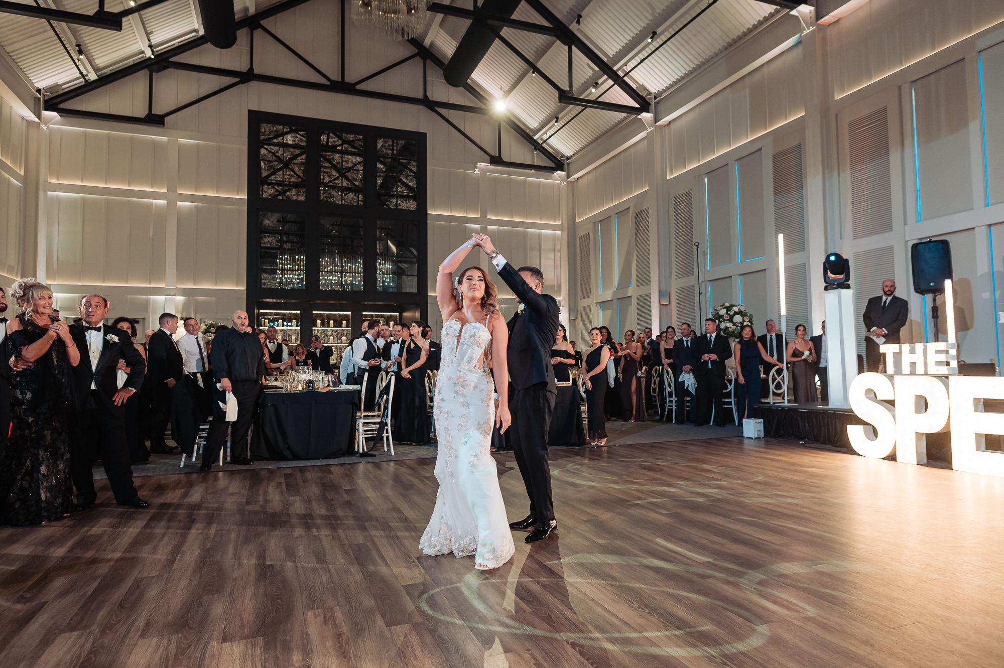 Bride and groom spinning during first dance framed by cheering guests and marquee sign