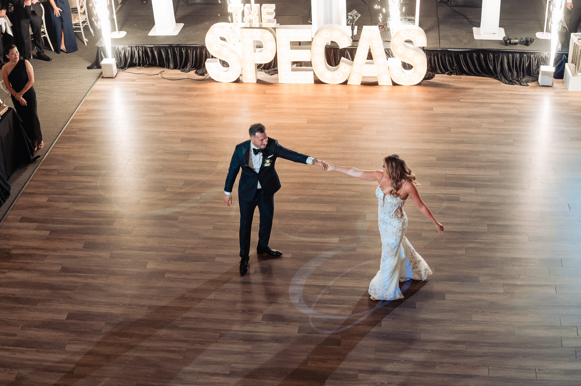 High-angle shot of bride and groom sharing a first dance on spacious wooden dance floor in front of marquee letters