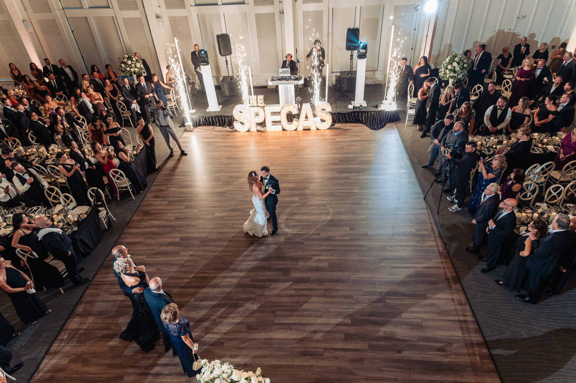 High overhead wide view of bride and groom first dance surrounded by guests and cold spark fountains