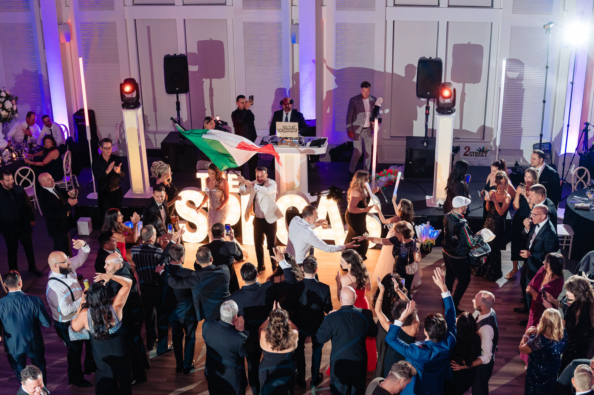 High-angle shot of reception crowd gathered around dance floor as groom waves Italian flag