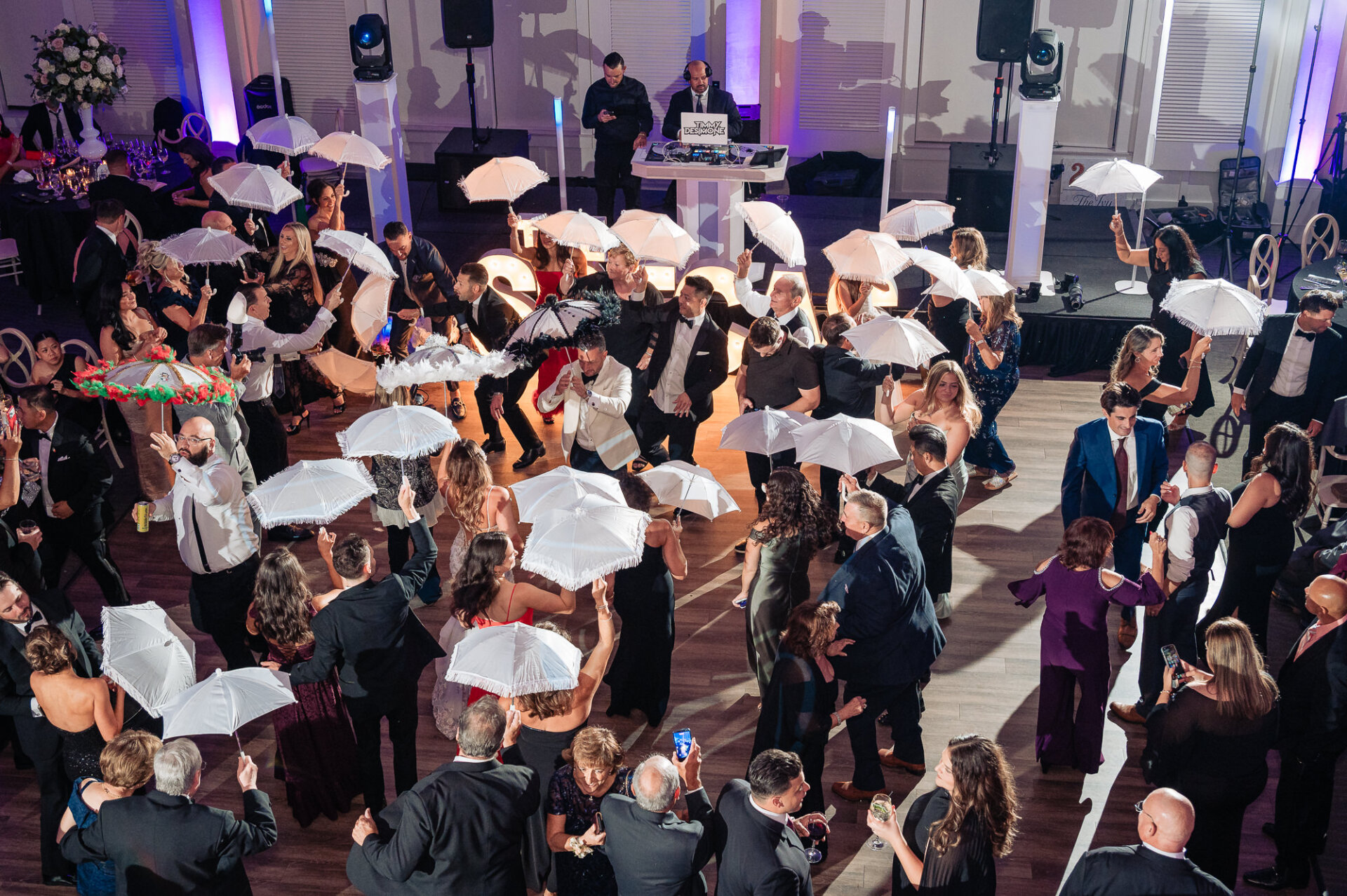 High-angle shot of wedding reception crowd dancing together while twirling white lace parasols