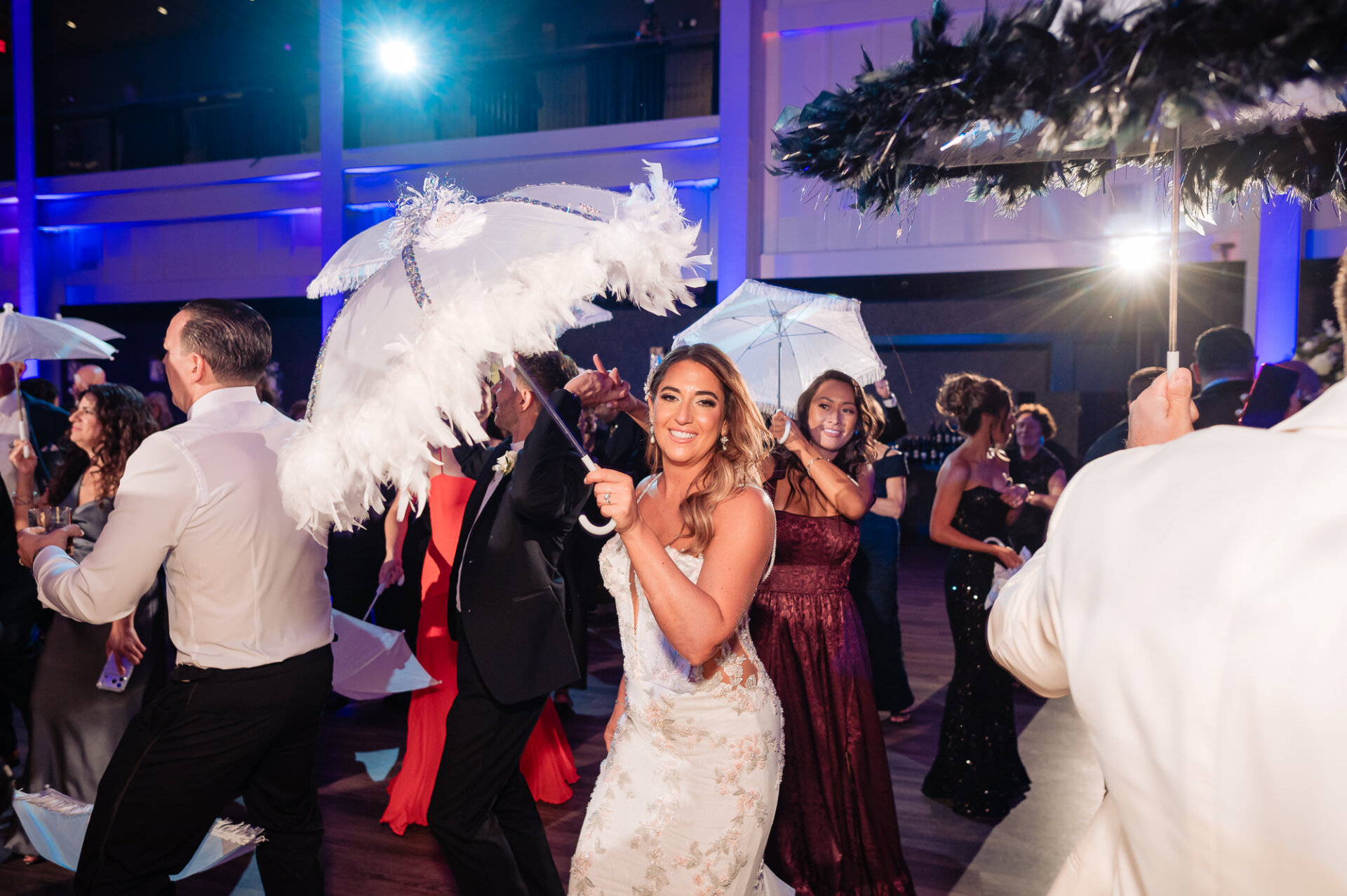 Bride smiling while dancing on packed dance floor twirling a white feathered parasol