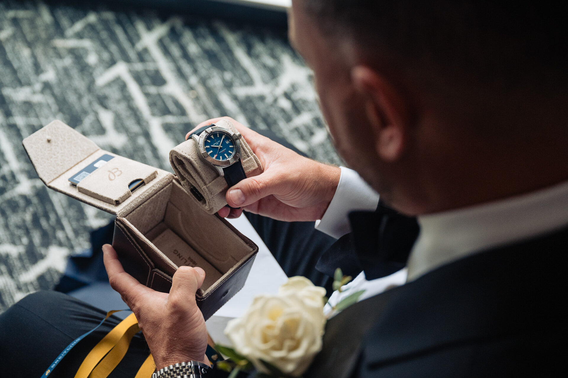 Groom holding blue-faced Breitling watch and leather travel case