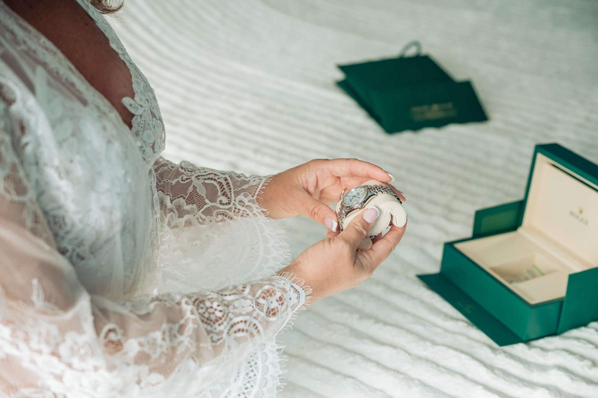 Bride holding a luxury silver watch gift next to green Rolex box on white bedspread