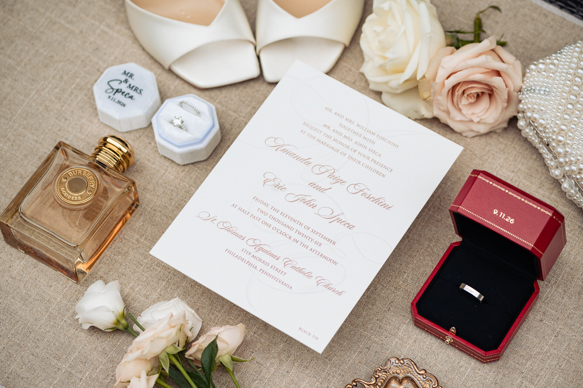 Flat lay of wedding invitation suite, Burberry perfume, bridal shoes, and Cartier ring boxes