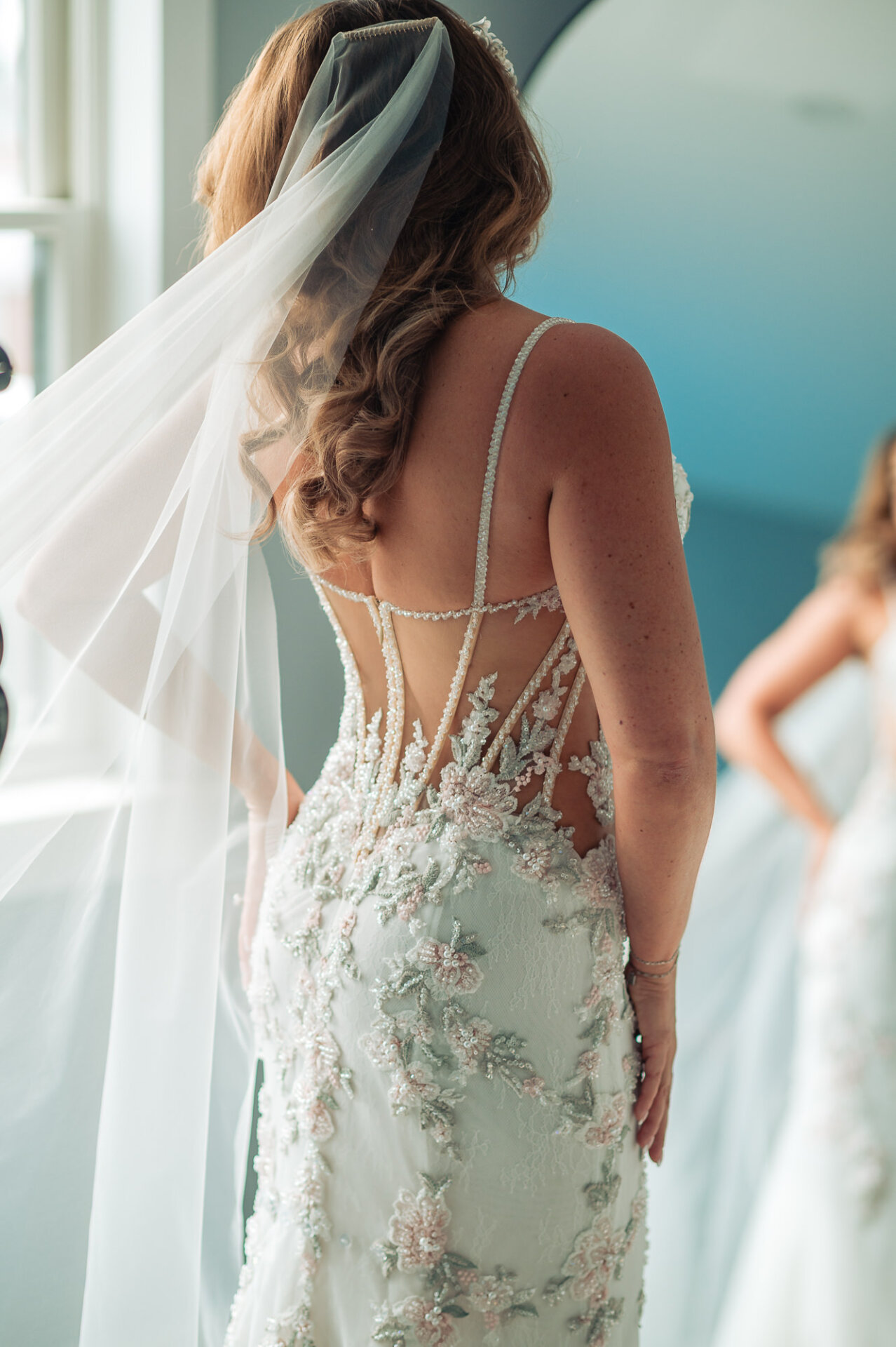 Back detail view of bride's sheer corset wedding dress with floral embroidery and veil