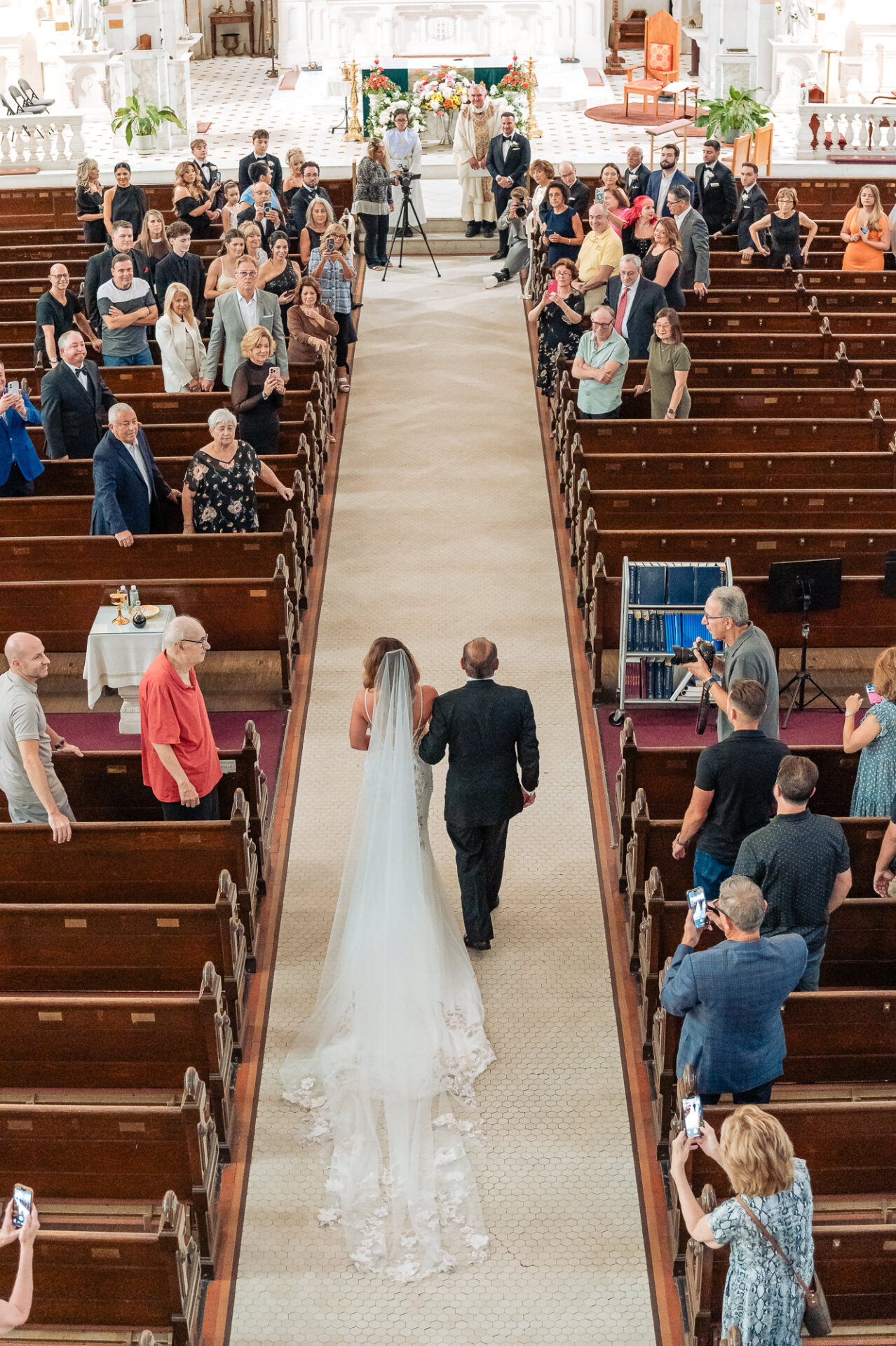 Overhead view of bride walking down church aisle with her father toward groom at altar during wedding ceremony