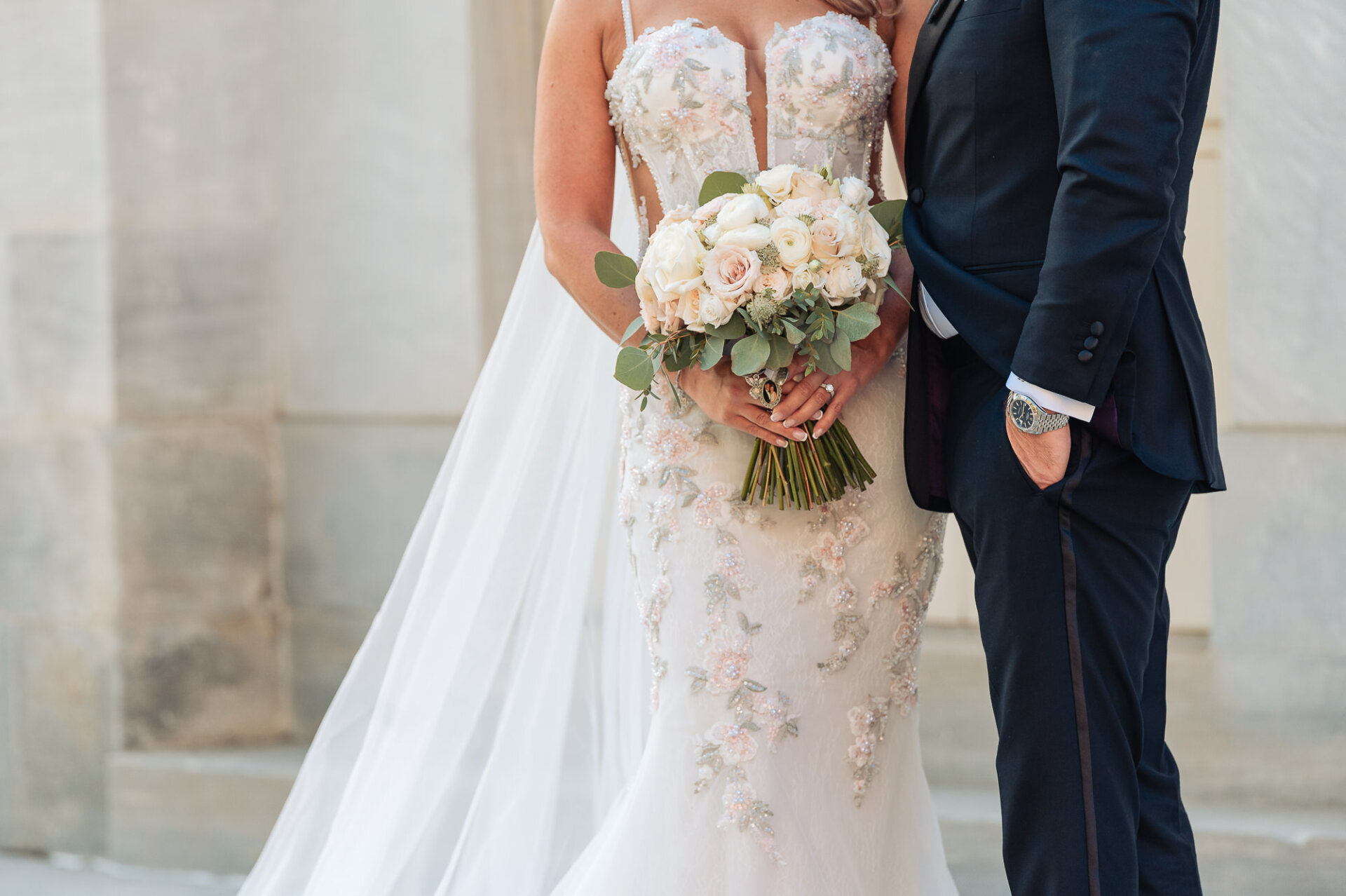 Close-up details of bride holding pastel rose bouquet standing beside groom