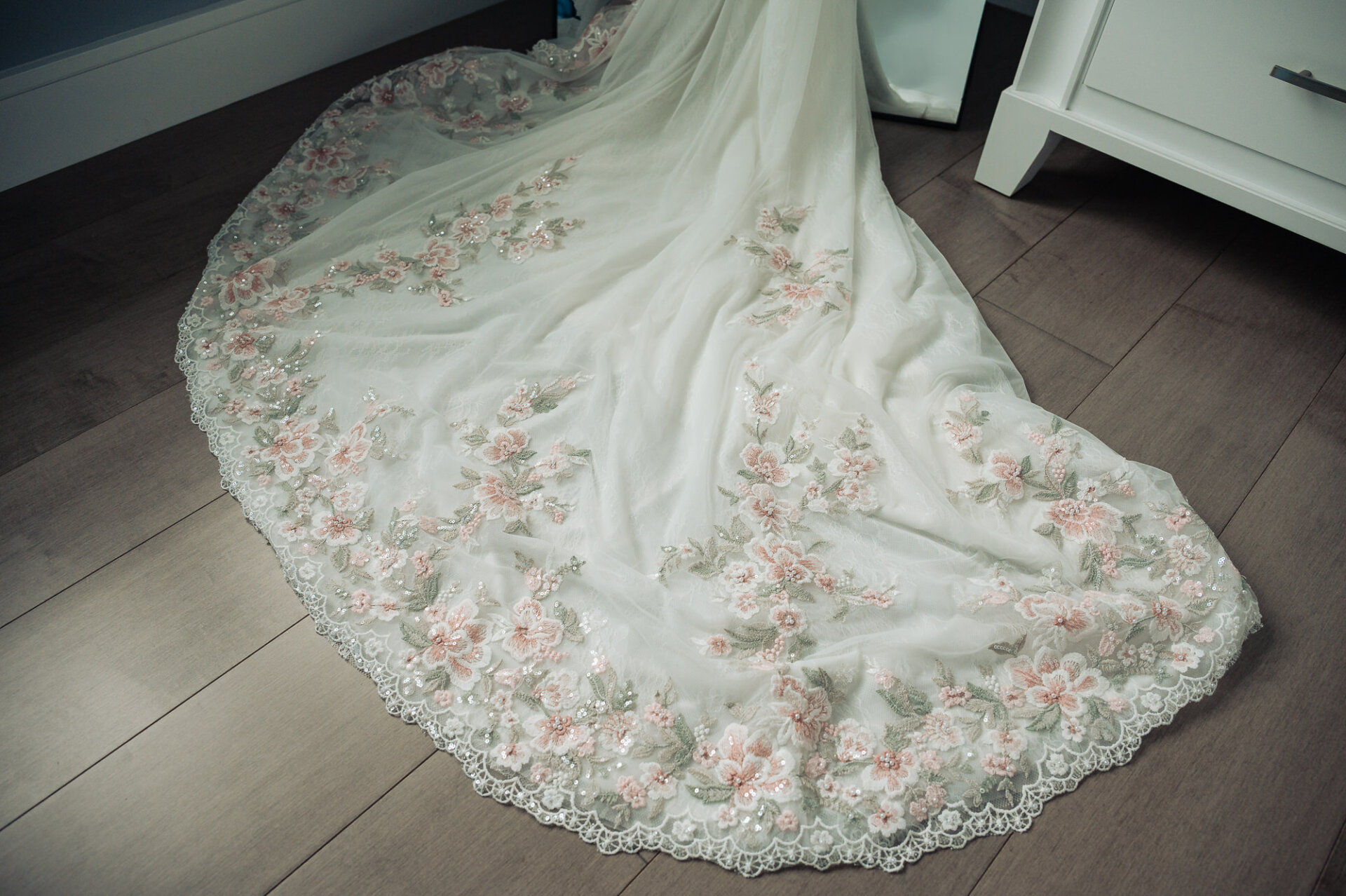 Detail view of floral embroidered wedding dress train spread out on wooden floor