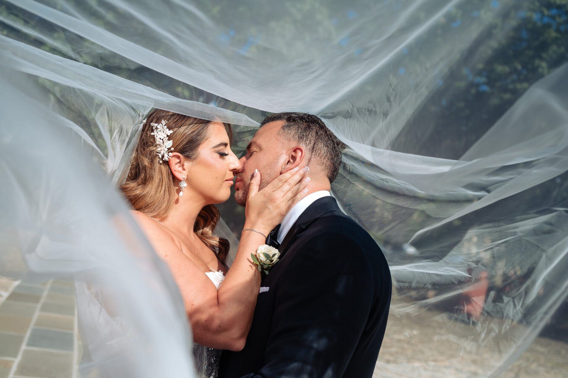 Close-up profile of bride and groom sharing intimate kiss wrapped under long veil
