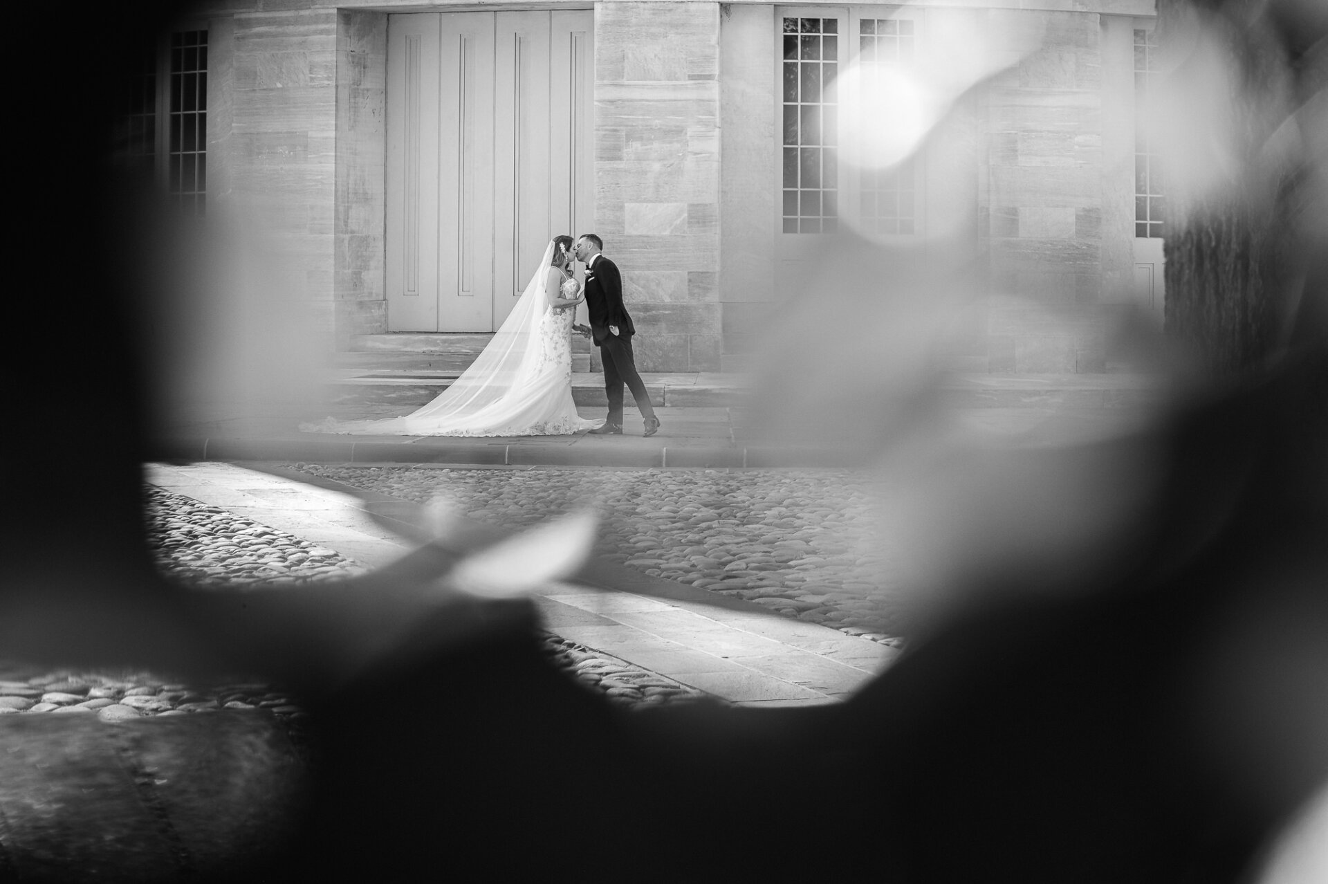 Framed shot of bride and groom sharing kiss on stone steps in front of classic building