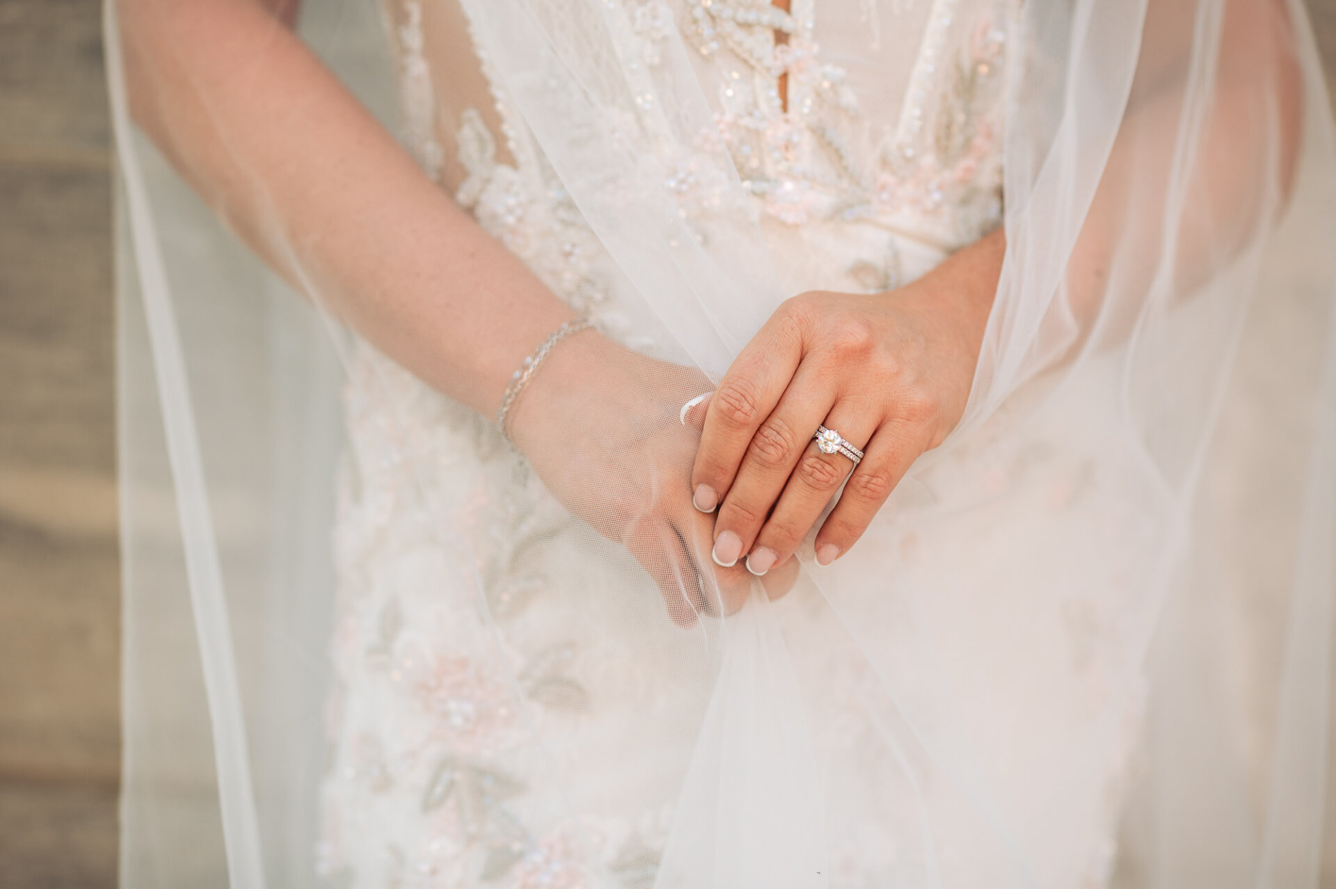 Close-up of bride resting hands over delicate veil showcasing diamond engagement ring and wedding band
