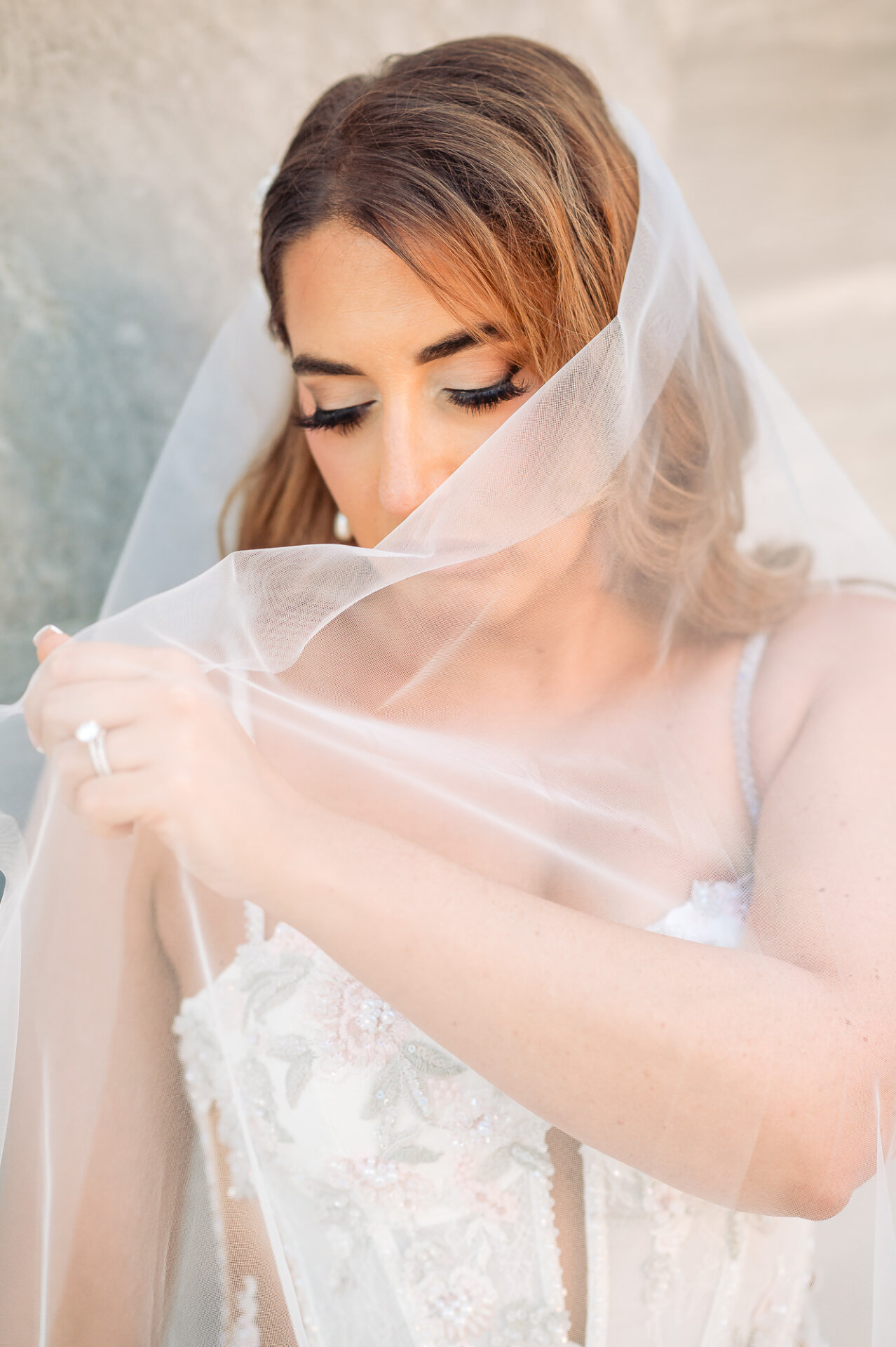 Close-up portrait of bride with eyes closed gently holding bridal veil over her face